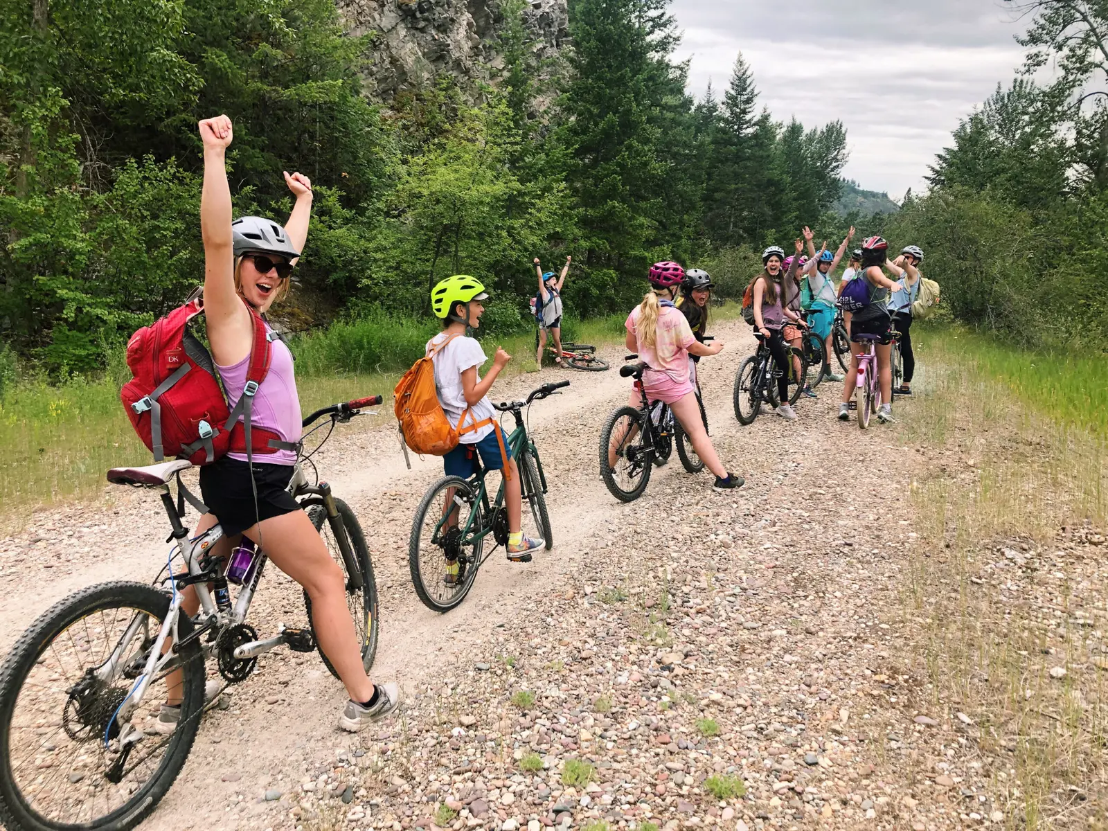 A group of people wearing helmets are biking on a gravel trail outdoors.
