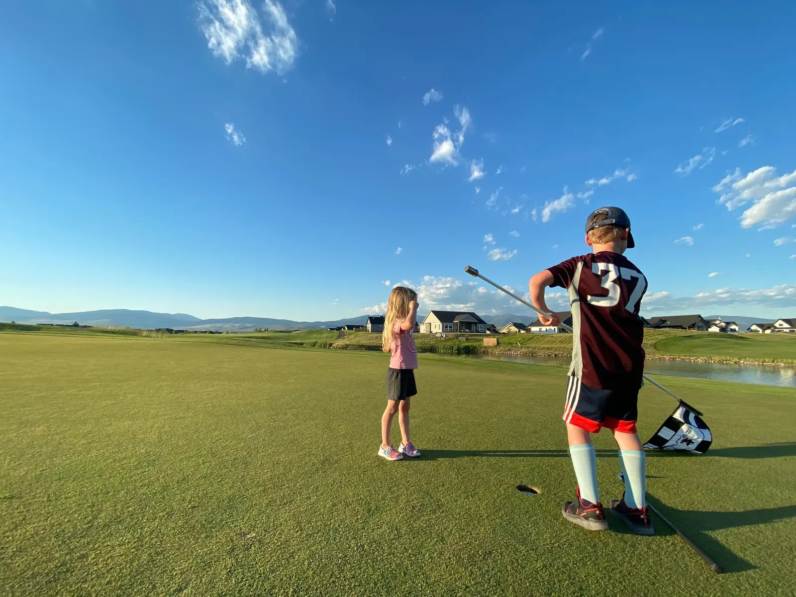 Two children are on a golf course, with one holding the flagstick.
