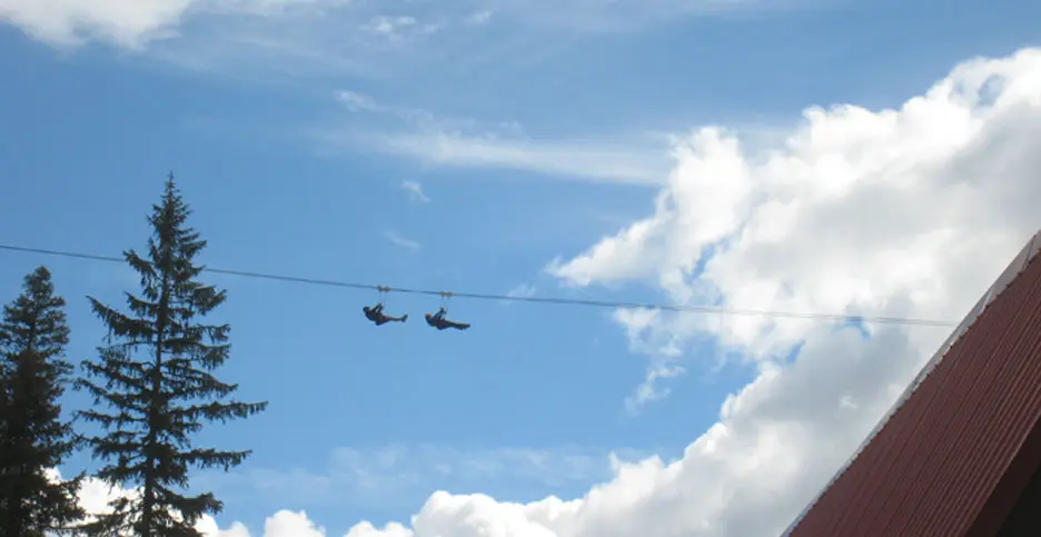 Two people ride a zip line across the sky.