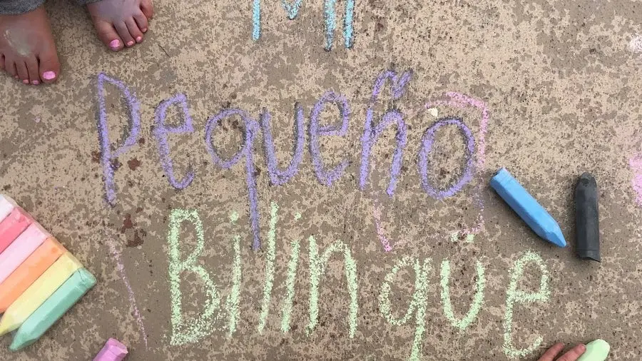 A person's feet stand beside sidewalk chalk writing that says Pequeño Bilingüe.