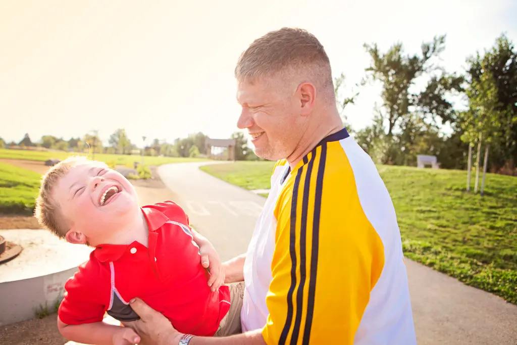A man holds a young boy who is laughing in an outdoor setting.