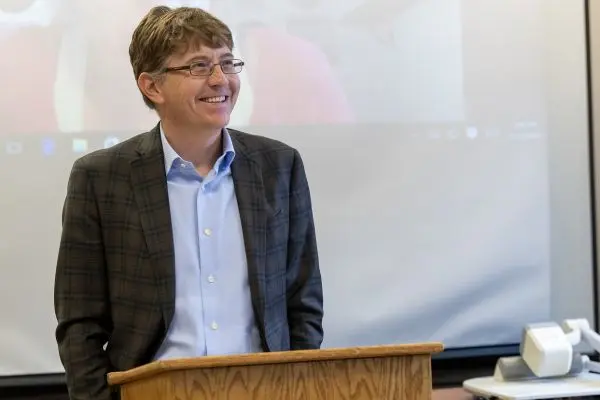 Man with glasses is smiling and giving a speech