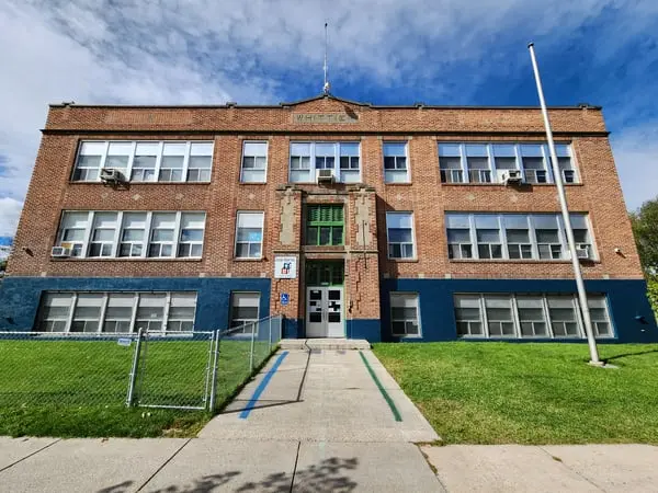 A brick school building stands under a partly cloudy blue sky.