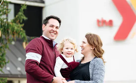 A family of three smiles while posing together outdoors.