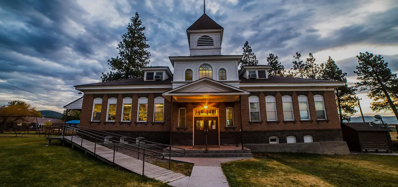 A historic brick school building with a wheelchair ramp stands under a cloudy sky.