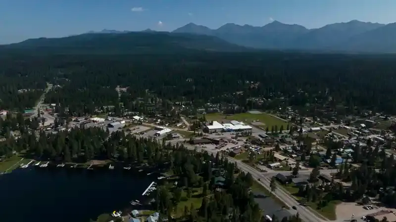 An aerial view captures a town situated near a lake with mountains in the background.