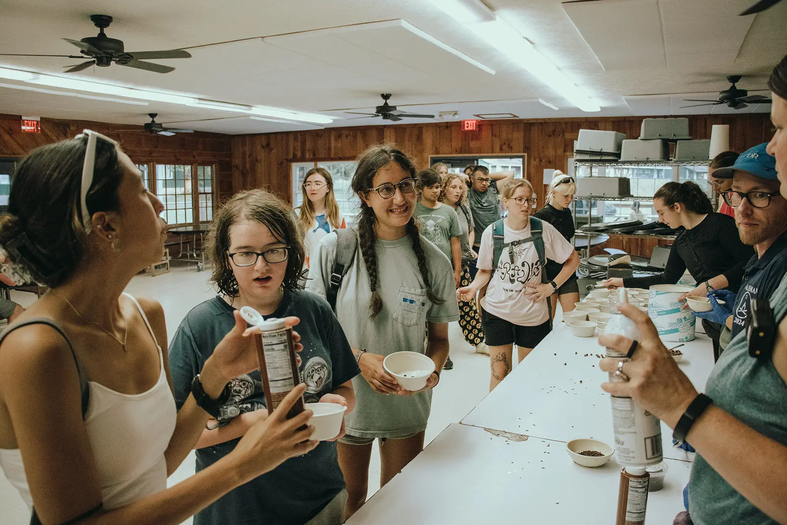 A group of young people and an adult staff member interact around a table with bowls and toppings.