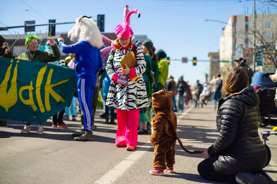 Person in zebra coat and flamingo hat smiles at kid dressed as animal.