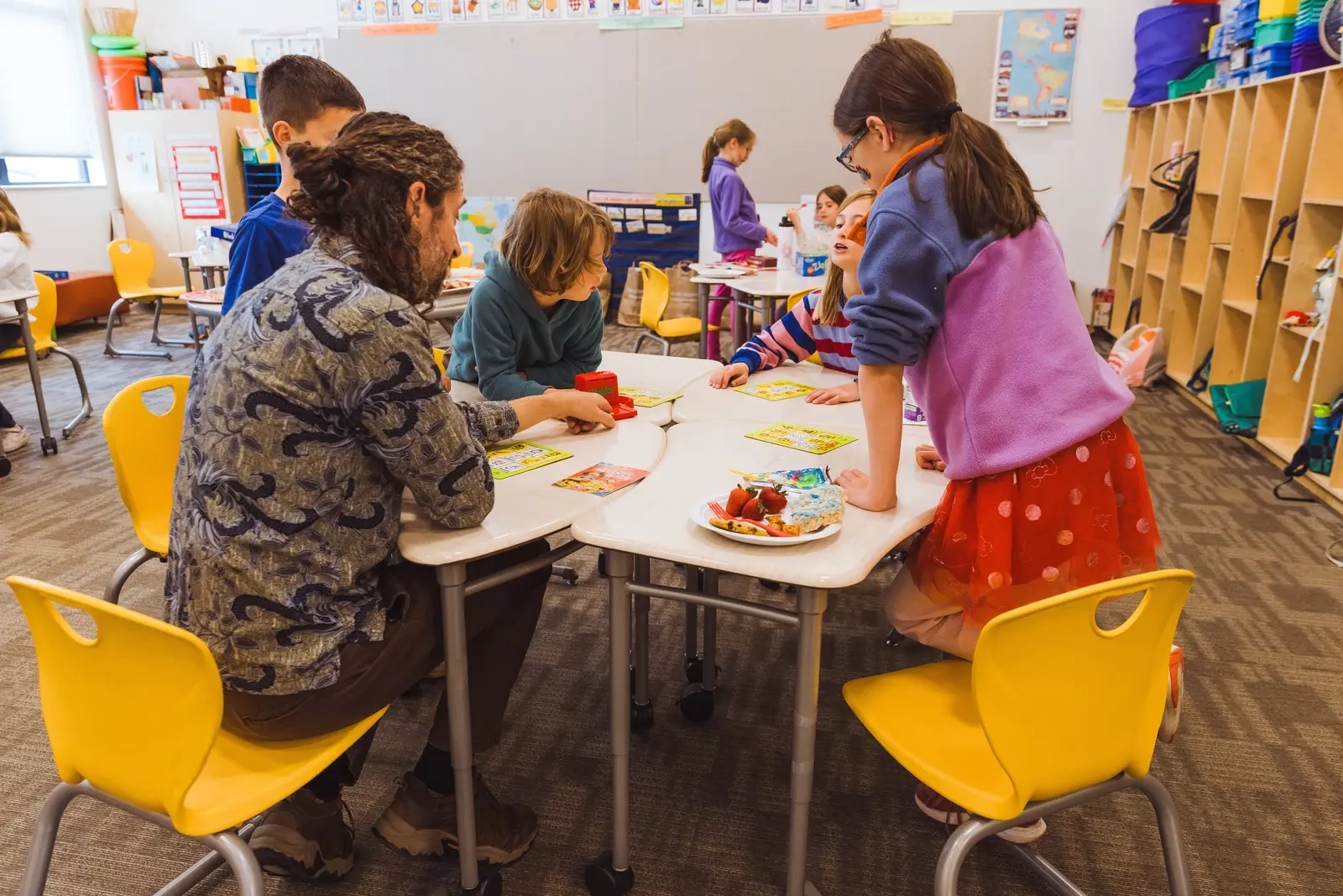 An adult instructor guides children as they play a board game together in a classroom.