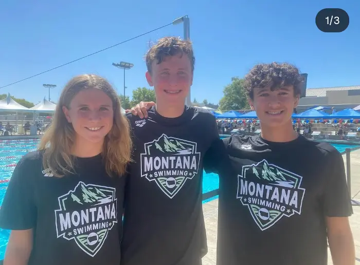 Three teenagers stand together in matching shirts at a swimming facility.