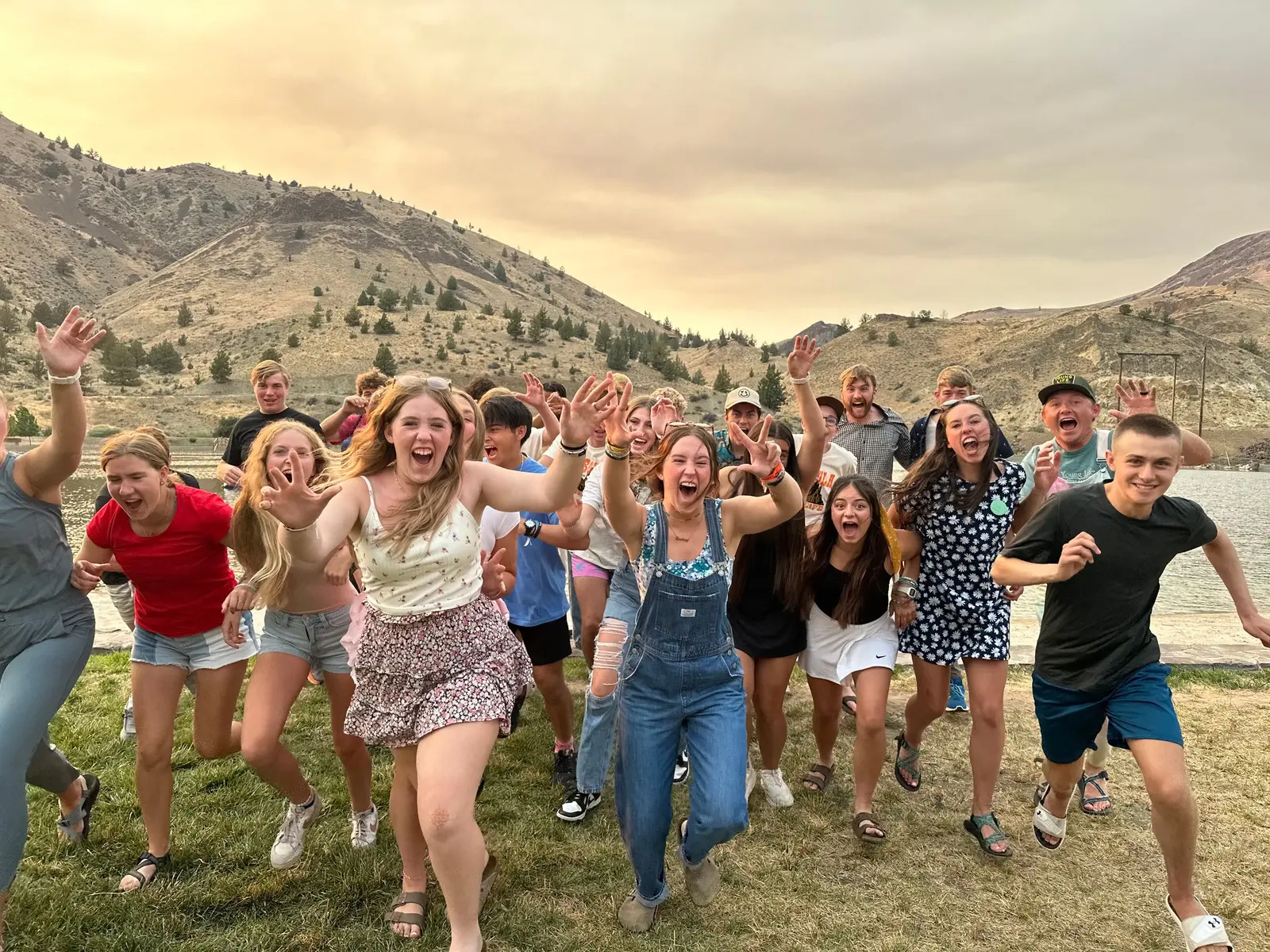 A group of young people run enthusiastically toward the camera outdoors with mountains in the background.