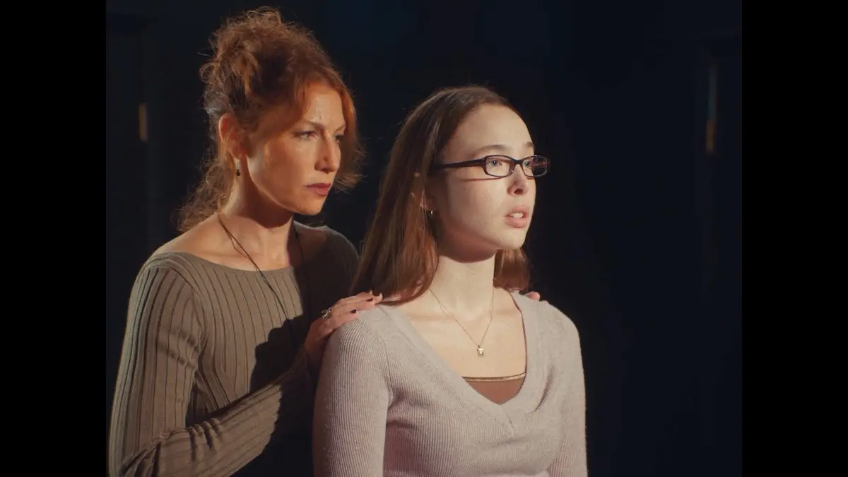 An older woman stands behind a younger woman with her hands on her shoulders.