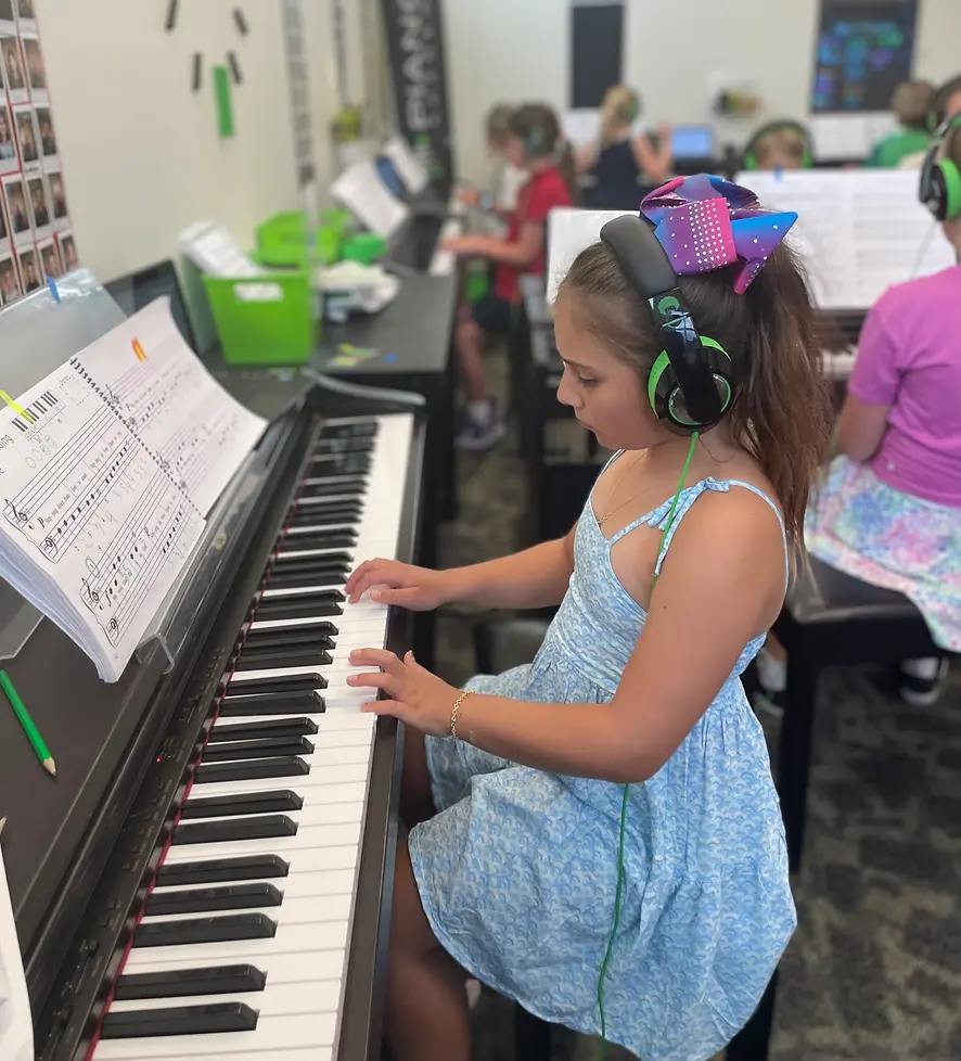 A young girl plays the piano while wearing headphones in a music classroom.