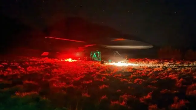 A helicopter is parked in a field at night, illuminated by red lights.