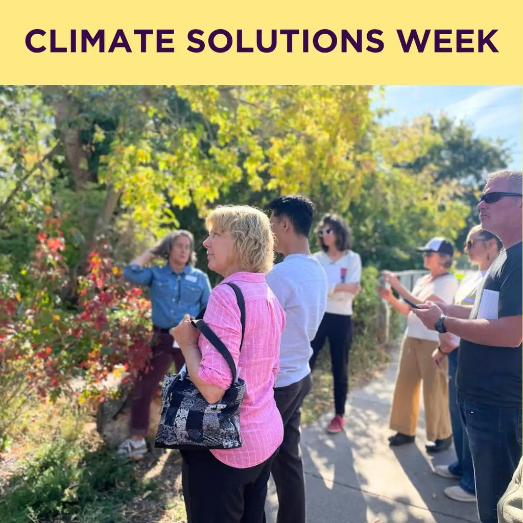A group of adults stand outside listening to a speaker during a climate solutions event.