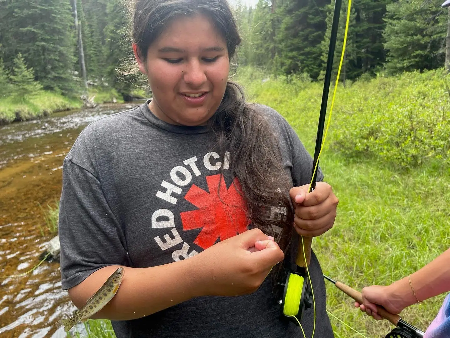 A person holds a caught fish while fly fishing outdoors.