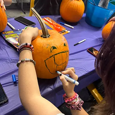 Teen drawing a face on a pumpkin