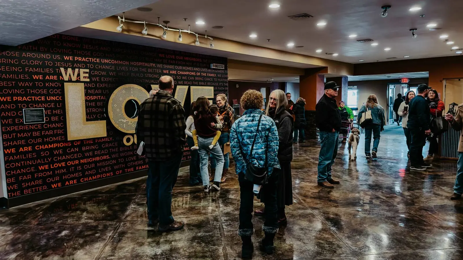A group of people gathers in a modern building lobby with a large mural on the wall.