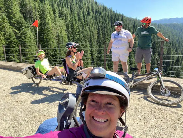 Smiling woman selfie on sunny day with people using various adaptive bikes behind her