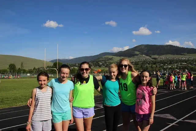 A group of young girls poses together on a running track with mountains in the background.