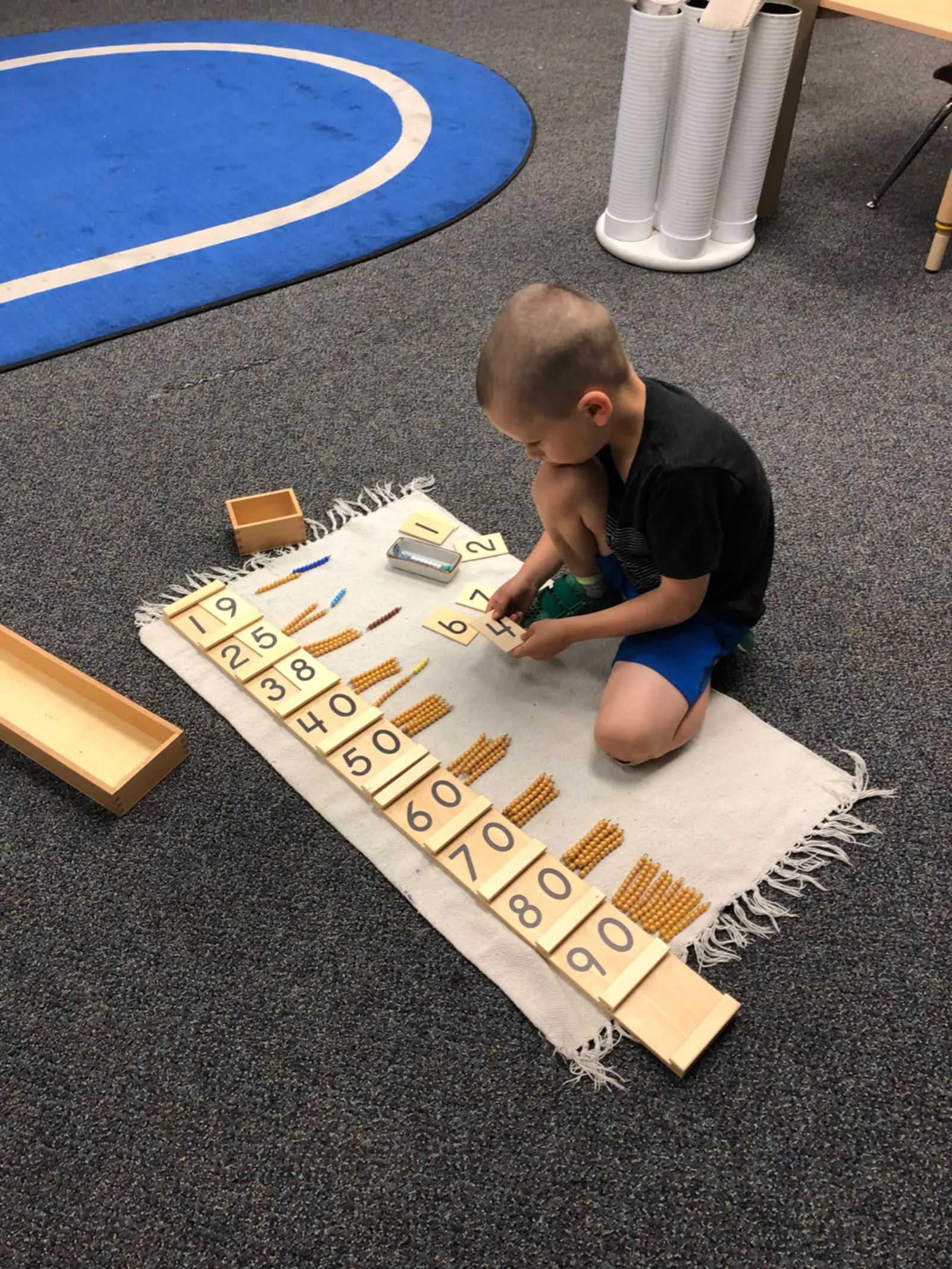 A child is actively learning with number tiles and bead counting materials on a rug.