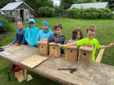 Photo from turnerfarms406.com A group of children work on building birdhouses outdoors at a wooden table.