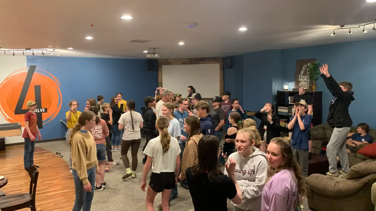 A large group of young people gather in a room with blue walls and a large logo.