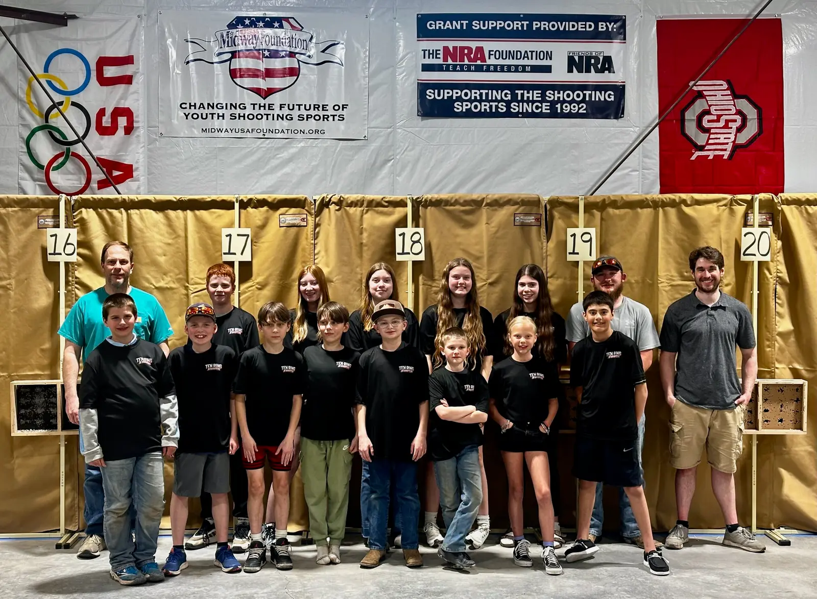 A group of young people and their instructors stand in a shooting range.