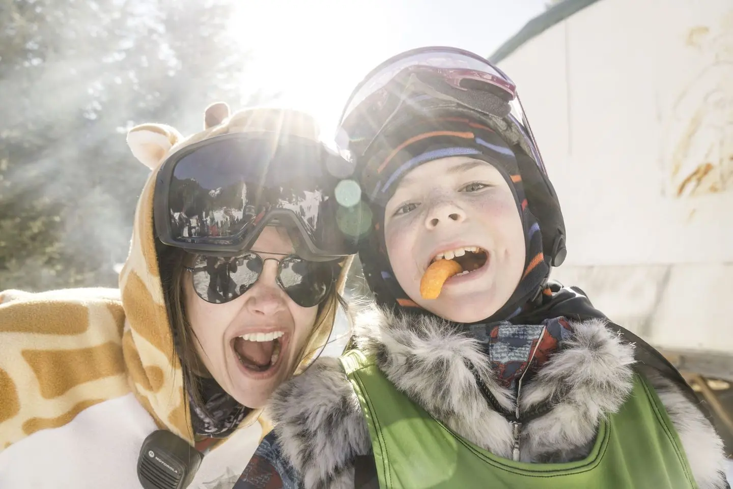 A person in a giraffe hoodie and a child wearing winter gear pose together outdoors.
