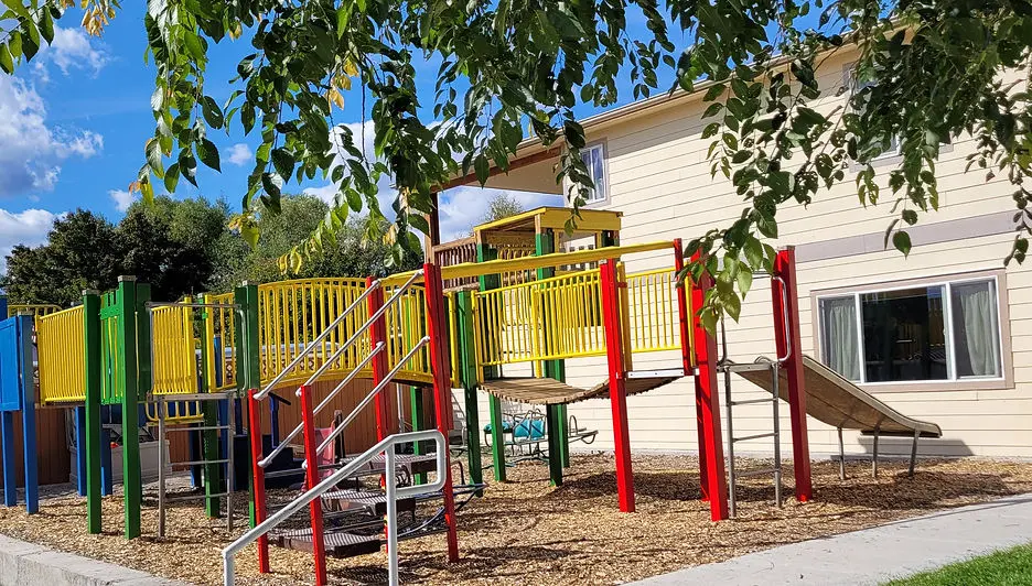 A colorful playground structure sits in a yard next to a beige building.
