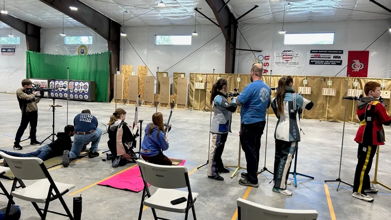 A group of people are practicing shooting in an indoor range under the guidance of an instructor.