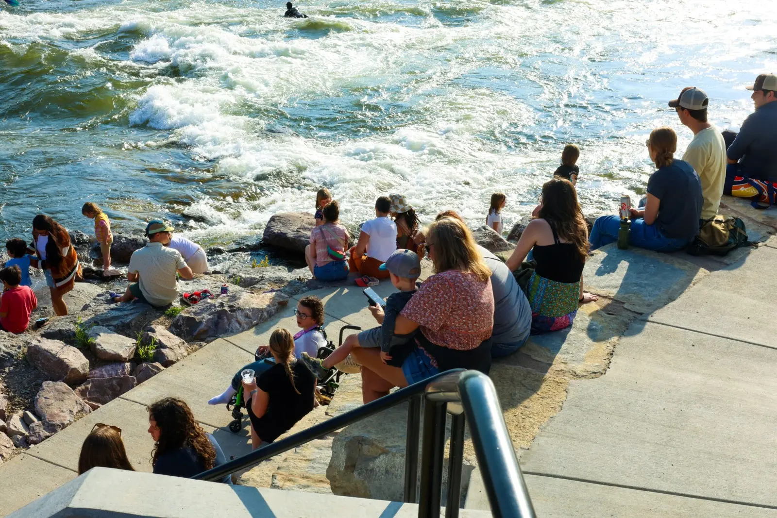 A group of people sit on stone steps overlooking a turbulent river.