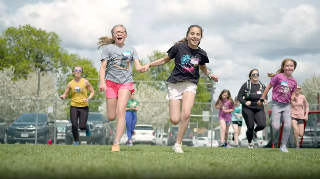 A group of children and adults are running together on a grass field.