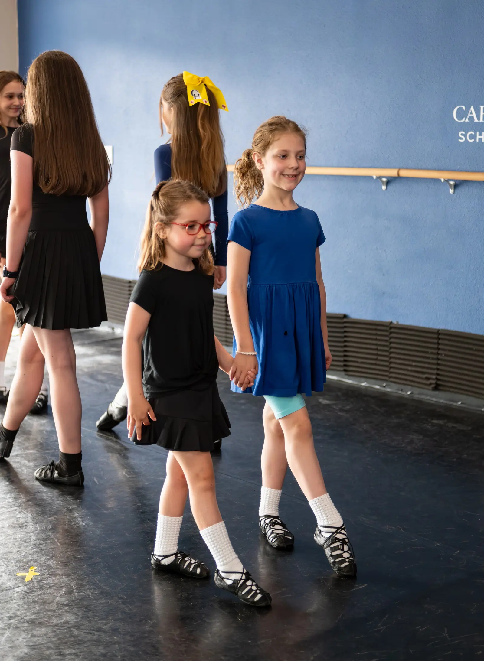 A group of children in dance attire practice steps together in a studio.
