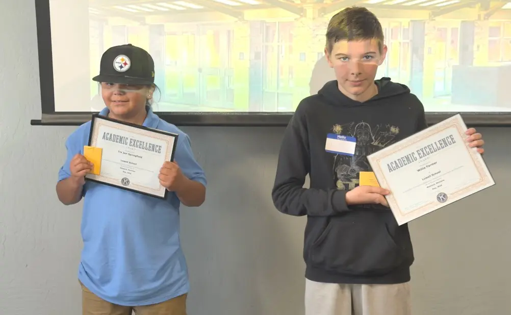 Two students stand side by side holding academic excellence awards.