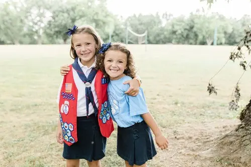 Two girls smiling and standing together outdoors in an open field.