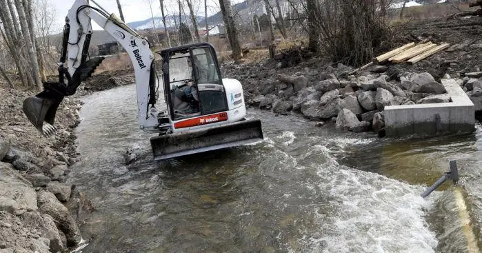 An excavator is working in a small creek to improve the stream bank.