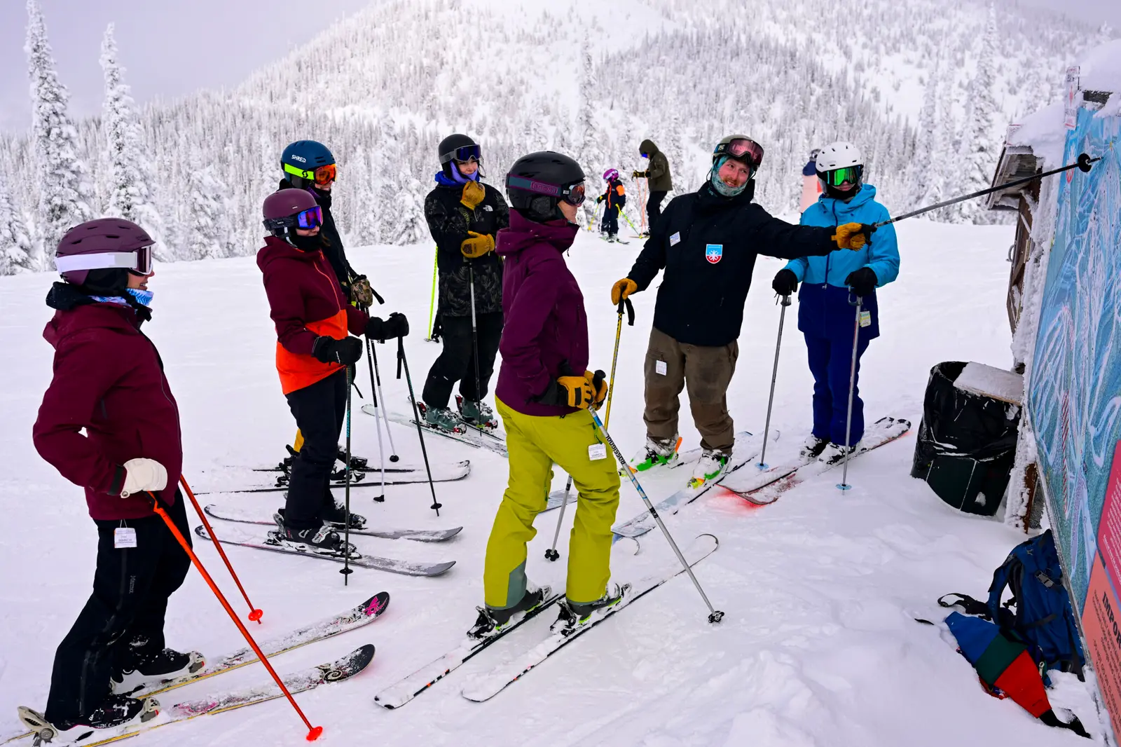 A ski instructor points to a trail map while teaching a group of skiers on a mountain.