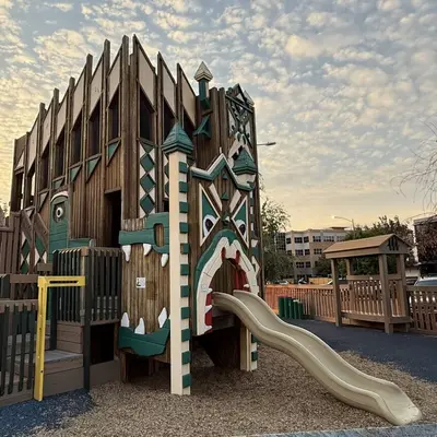 Photo from missoulacarousel.org A large wooden playground structure with a slide outdoors.