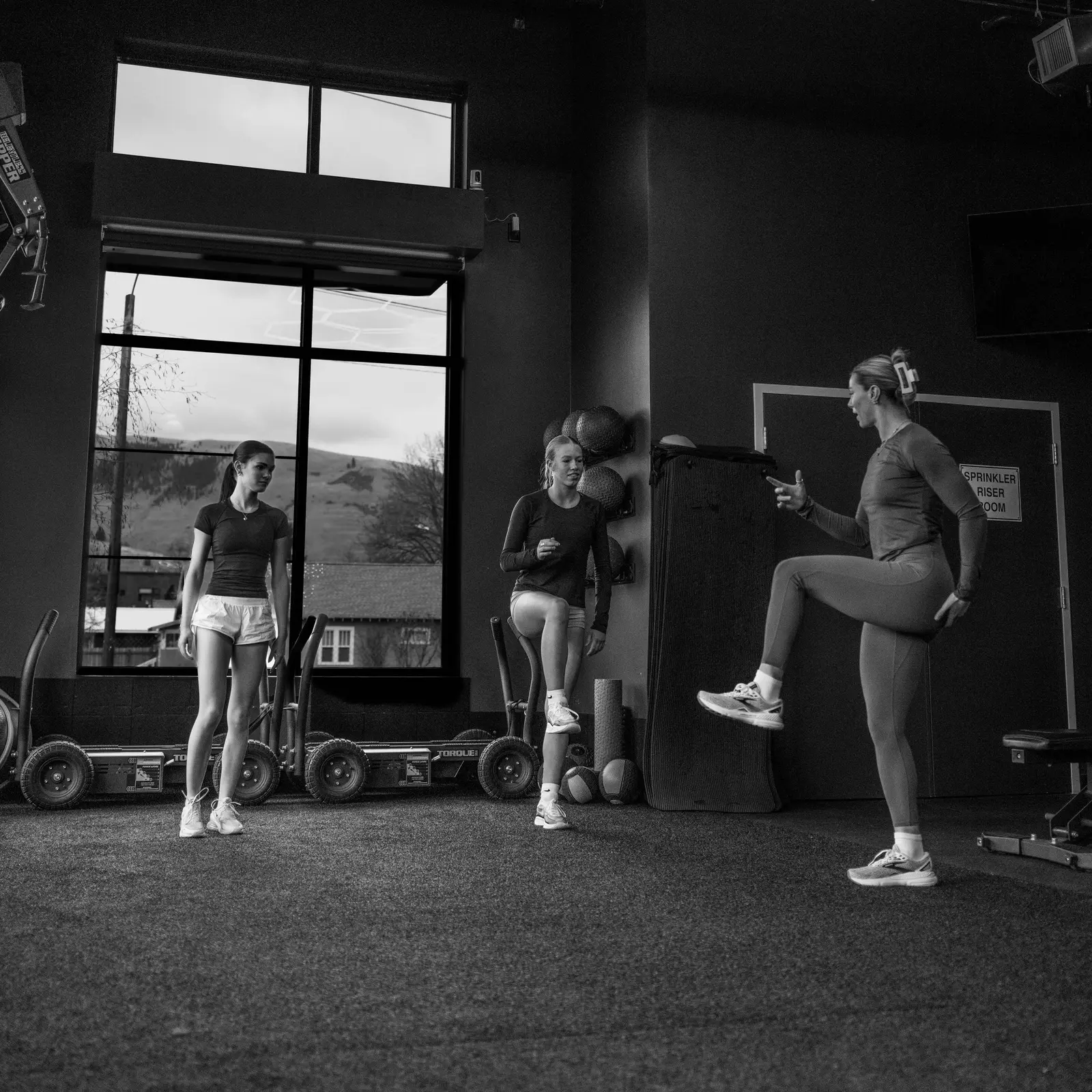 An instructor leads two other women through a fitness exercise in a gym.