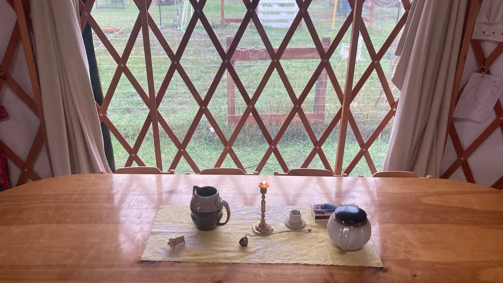 A wooden table inside a structure with lattice walls holds a small candle and some ceramic dishware.