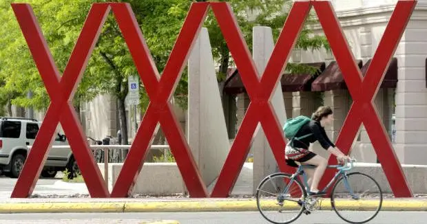 A person rides a bicycle in front of a large, red, X-shaped sculpture.