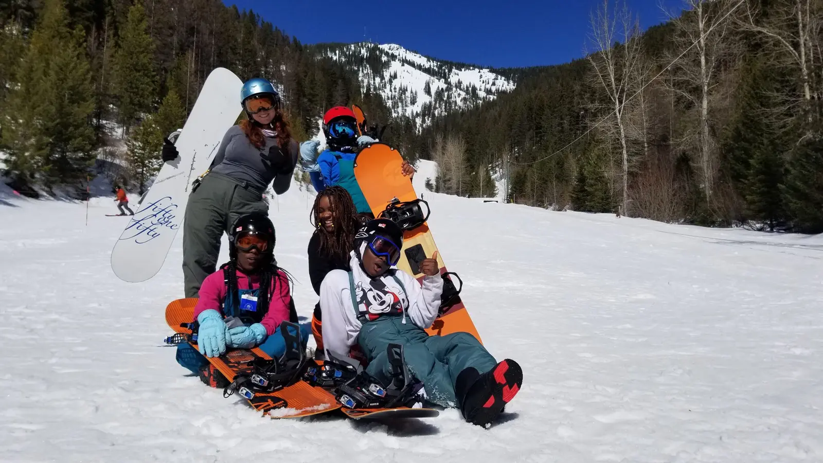 A group of snowboarders sits together on the snow at a ski resort.