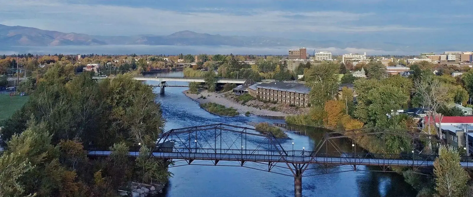 An aerial view shows a river flowing through a city with bridges and fall foliage.