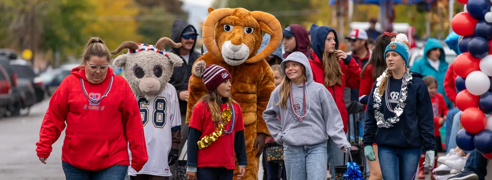 A group of children, an adult, and a mascot walk together during an outdoor parade.