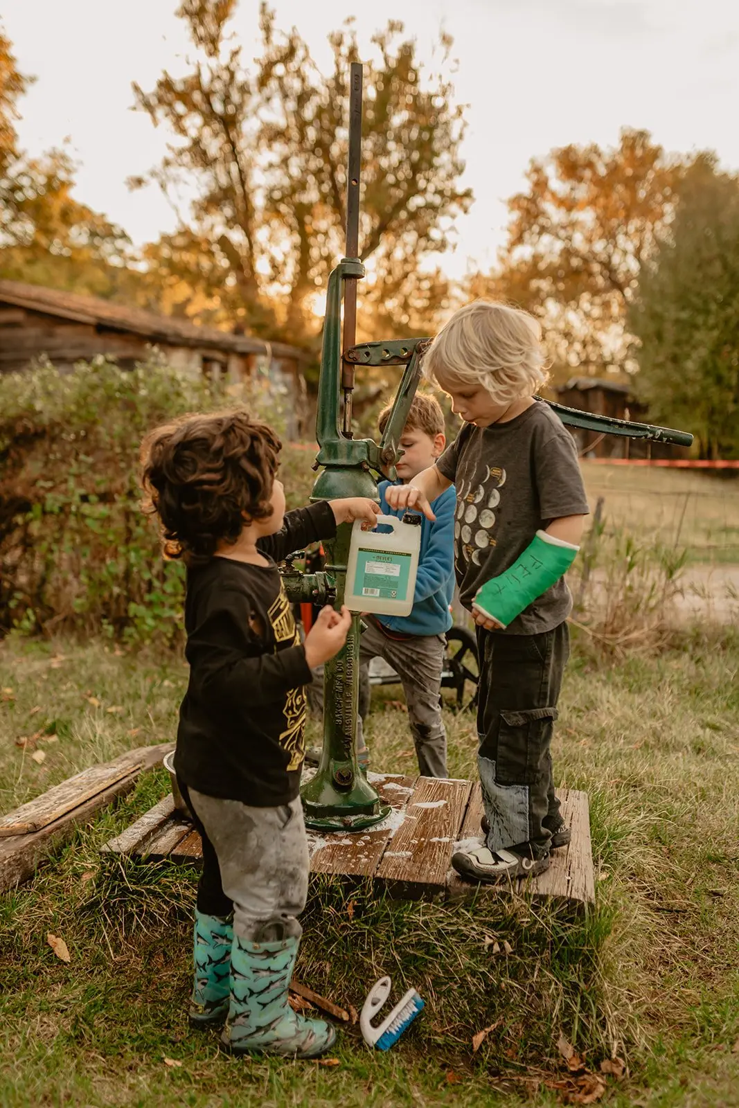 Three young children interact with an outdoor water pump.