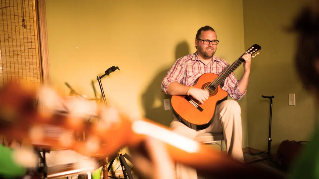 A man plays an acoustic guitar while sitting in a room.