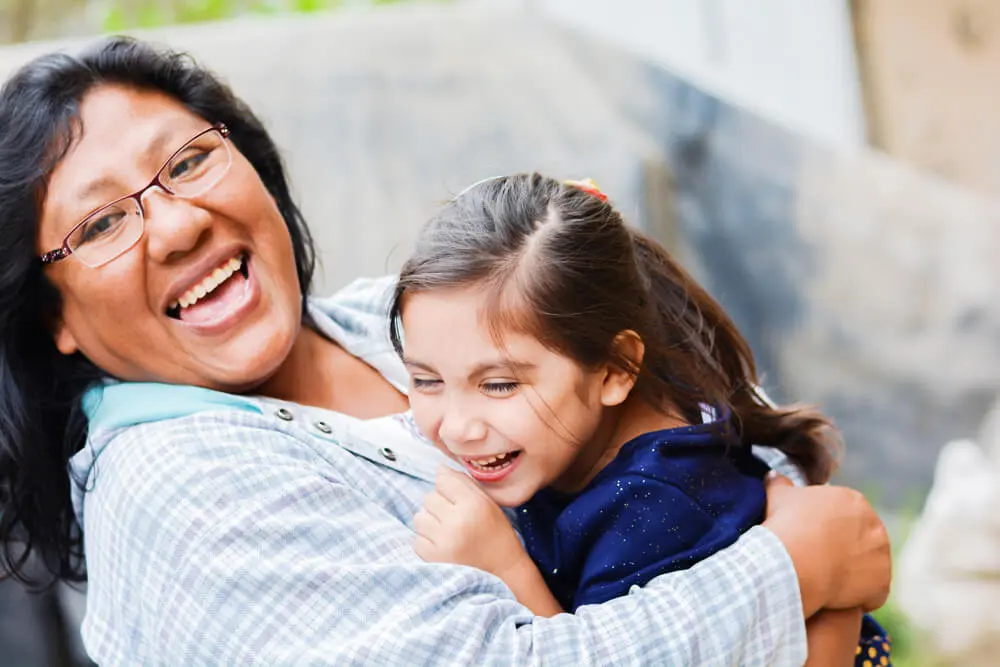 A woman smiling and hugging a young girl who is also laughing.
