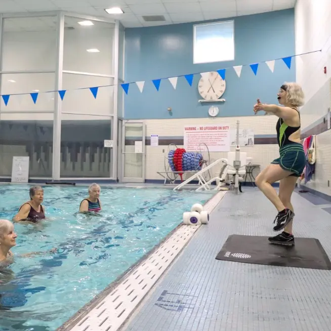 An instructor leads a water aerobics class at a pool with older adults.