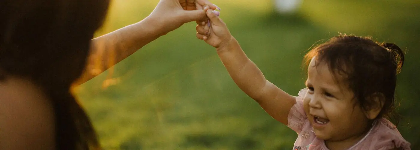 A child reaches out to hold hands with an adult in a grassy area.